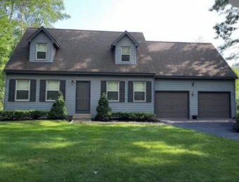 A cape style home with dormers and an attached garage under a finished brown shingle roof