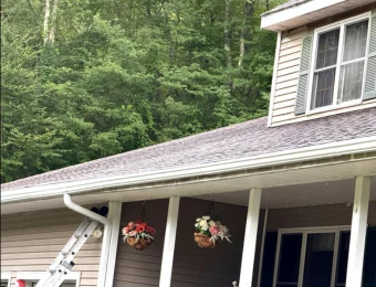 New shingle roof and gutter line above a covered porch, with a ladder still set against the eave