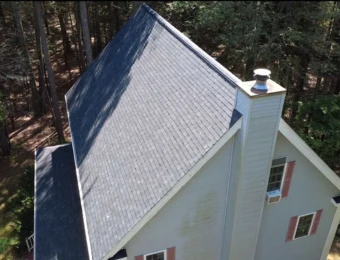 Overhead view of a newly shingled steep roof on a home surrounded by pines
